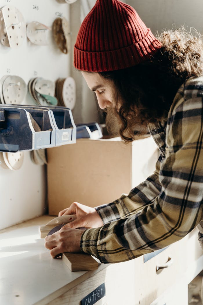 A focused craftsman using sandpaper on wood in a well-lit workshop.