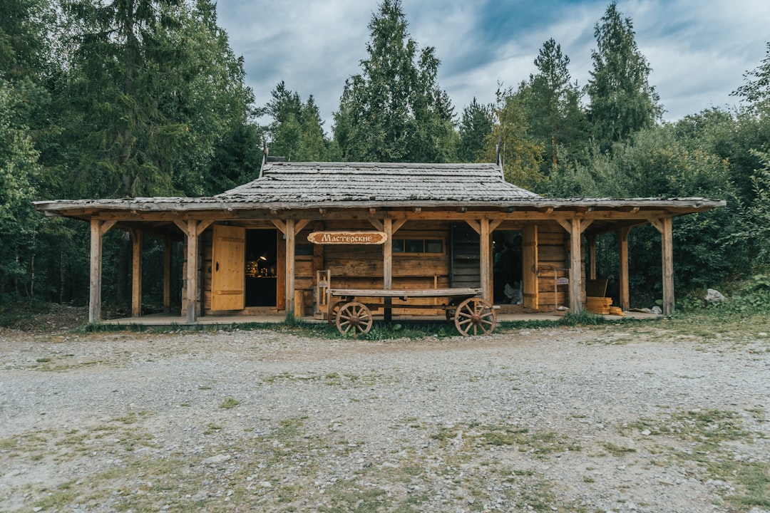 contact A rustic wooden workshop building in Ruskeala Mountain Park, Karelia. The structure, built in traditional northern style, stands surrounded by dense forest, with an old wooden cart adding to the authentic historical atmosphere of the site.