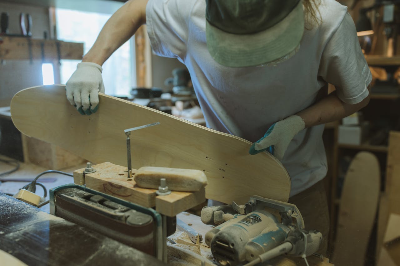 portfolio-01 Artisan shaping a wooden skateboard in a workshop with precision tools.