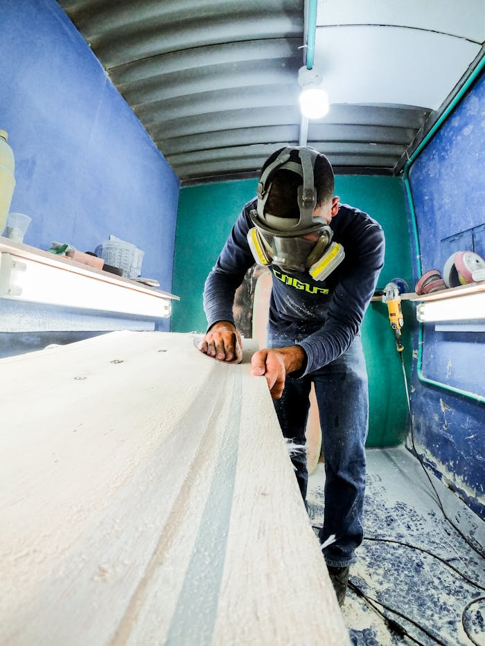 A craftsman wearing safety gear smooths wood in a well-lit workshop.